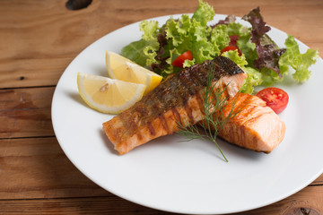 Grill salmon steak serve with lemon and colorful salad on wooden table