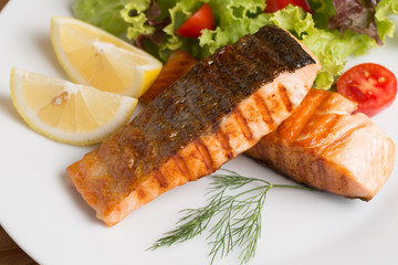 Grill salmon steak serve with lemon and colorful salad on wooden table