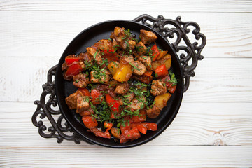 Tasty meat with vegetable on frying pan on white wood background