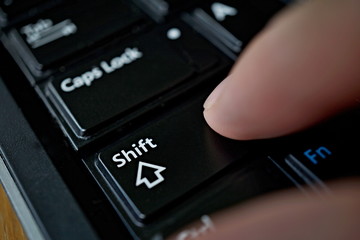 Side view of a male finger pressing black keys on the computer keyboard 