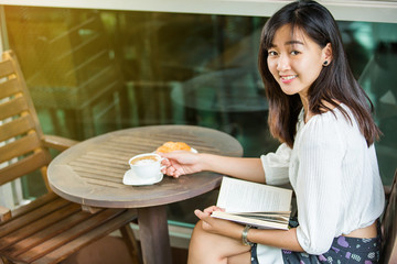 asian woman drink coffee and reading book in garden