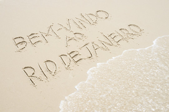 Wave approaches Brazil Bem-vindo ao Rio de Janeiro (Welcome to Rio) message in Portuguese handwriting in sand