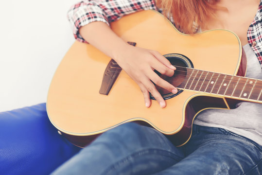 Beautiful young woman on sofa is playing guitar