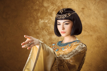 Beautiful Egyptian woman like Cleopatra pointing finger away on golden background - obrazy, fototapety, plakaty