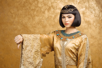 Serious Egyptian woman like Cleopatra with thumbs down gesture, on golden background