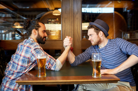 men drinking beer and arm wrestling at bar or pub