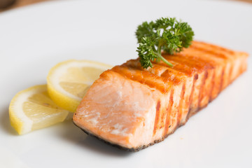 Grill salmon steak serve with lemon and colorful salad on wooden table