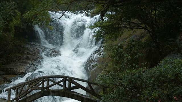 Whitewater cascades down its rocky course and under a small foot bridge at Datanla Falls near Da Lat, Vietnam, with sound. Footage UHD
