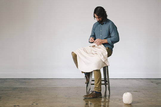 A male artist working, using string to crochet and create an art piece.