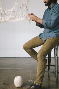 An artist seated working on an art piece, woven fabric and thread.