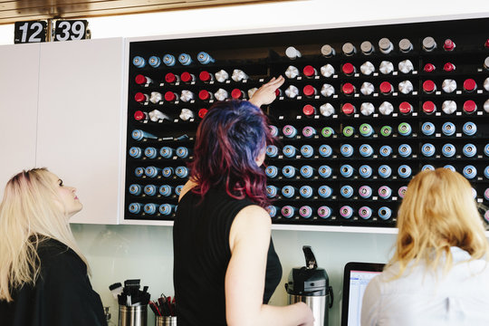 A woman reaching up to select a ground coffee pod to use to maker a morning coffee in the kitchen of the hair salon. 
