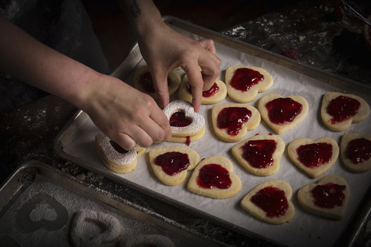 Valentine's Day baking, woman spreading raspberry jam on heart shaped biscuits