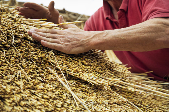 Close up of a man thatching a roof, layering the straw.