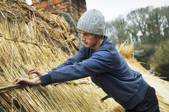 Thatcher standing on a roof, fastening straw at a seam.