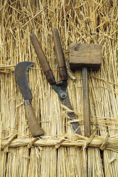 Close up of wooden mallet, shears and bill hook on straw thatched roof