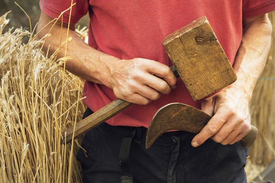 Close up of a thatcher holding a bill hook and wooden mallet.