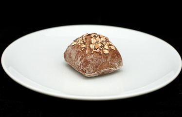 Rye sandwich bun with cereals on white plate 