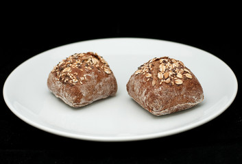 Two rye sandwich buns with cereals on white plate
