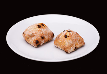 Two sandwich buns with raisons on white plate