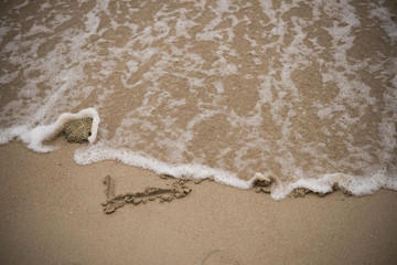 love handwritten on a sandy beach with wave on background