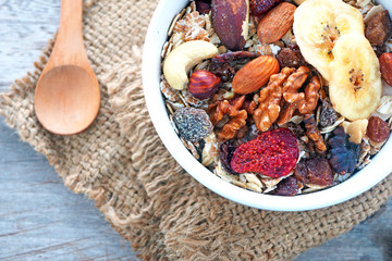 Top view of a healthy bowl of muesli with dried fruit and nuts on a wooden table.
