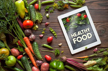 Tablet with text "Healthy food" Fresh organic Vegetables on Wooden Background. Healthy Vegetarian food, View from above.