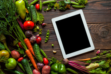 Tablet with black screen. Fresh organic Vegetables on Wooden Background. Healthy Vegetarian food, View from above.