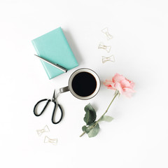 black coffee mug, pink rose, scissors, golden clips, mint diary and pen on white background. flat lay, top view
