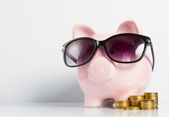 Piggy bank with sunglasses and coins on the white background