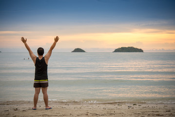 portrait of man standing on the beach at the day time and raising hands