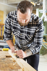 Carpenter work with plane on wood plank in workshop