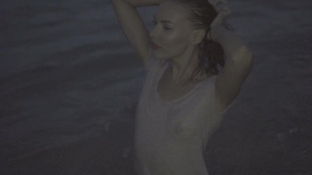 Beautiful blonde sexy woman wearing t-shirt posing in the sea during summer evening with wet hair - video in slow motion