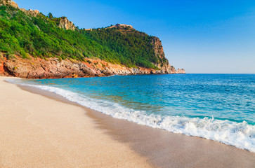 Fototapeta na wymiar Cleopatra beach with beautiful sand and green rocks in Alanya peninsula, Antalya district, Turkey, Asia. Famous tourist destination with high cliff and ancient old Castle. Summer bright day