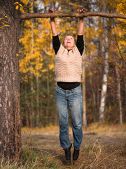 A woman in a sweater and jeans pulled to a branch on blurred background