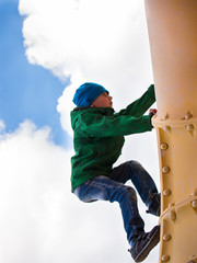 The child in a cap and jacket pipe climbs up on a background cloudy sky