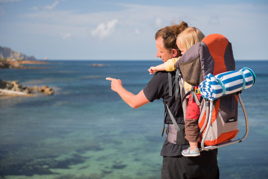 Father and baby in backpack carrier outdoors near the sea