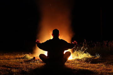 Silhouette of a man sitting in the lotus position at night by th