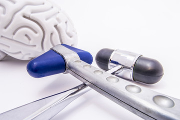 Two chrome neurological hammer with blue and black heads crosswise on a white medical table against of the brain figures in the background