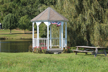 white gazebo in a park with pond and picnic table