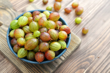 Fresh ripe gooseberries in bowl on a wooden background closeup