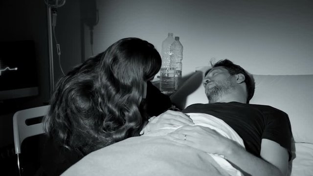 Sad woman crying in hospital holding hand of sick boyfriend at night black and white