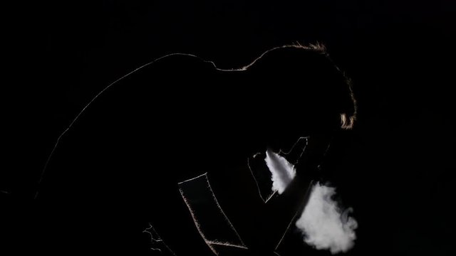 Brutal sad man sits and smokes an electronic cigarette. Black. Silhouette