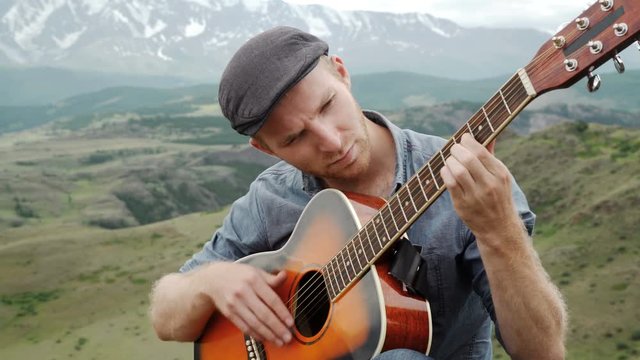 young guy playing guitar sitting on the grass