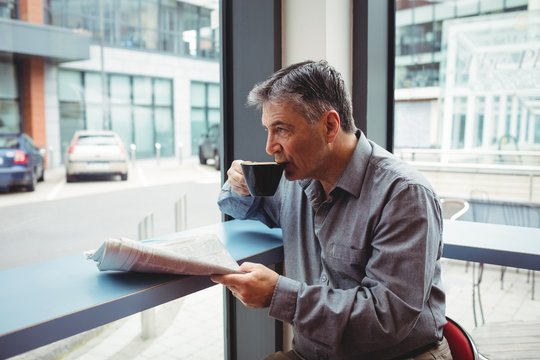 Man holding newspaper and having coffee