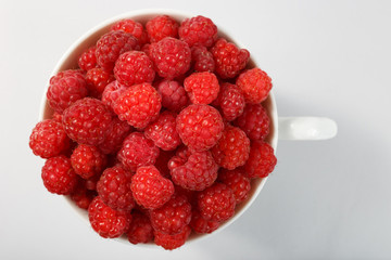 Top view of a white bowl filled with raspberries on a light background