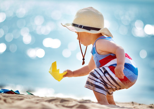 little boy playing at the beach in straw hat