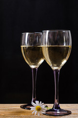 Two glasses of white wine on a wooden table with a chamomile on