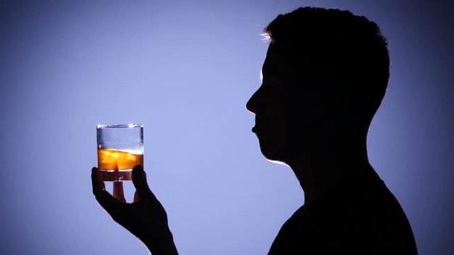 Man Drinks Whiskey With Ice. Close Up. Back Light