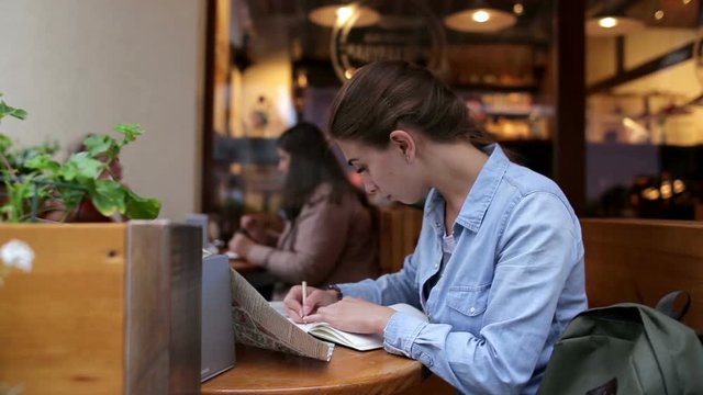 Young beautiful woman writes at cafe and looks at map