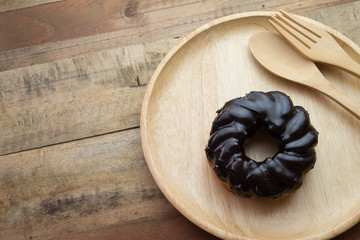 A chocolate glazed donut on wooden plate. Shot from above on wooden background.